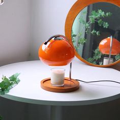 an orange lamp sitting on top of a white table next to a mirror and potted plant