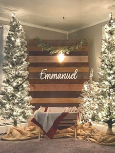 christmas trees and lights are arranged in front of a wooden sign that reads, emmanuel