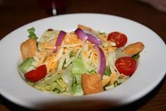 a white bowl filled with salad and croutons on top of a wooden table