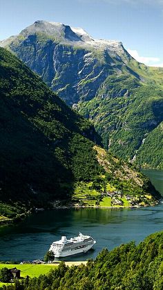 a cruise ship in the middle of a lake surrounded by mountains and greenery on a sunny day