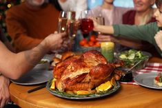 people sitting at a table with plates and glasses of wine in front of the turkey