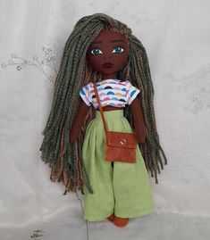 a doll with dreadlocks is posed on a white background, wearing a green skirt