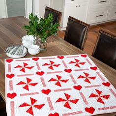 a quilted table runner with red and white hearts on it, sitting on a wooden dining room table