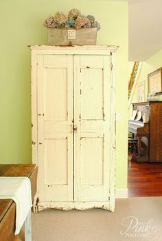 an old white armoire in a room with green walls and hardwood floors, along with a potted plant on top of the cabinet