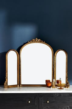 three mirrors sitting on top of a white counter next to a vase and candle holder