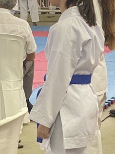 two women in white kimonos standing next to each other on a blue mat