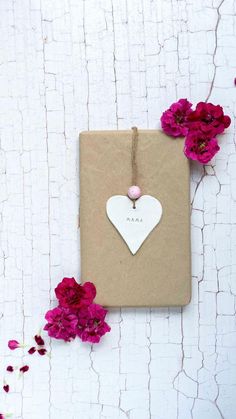 a brown paper bag with a white heart hanging from it's side next to pink flowers