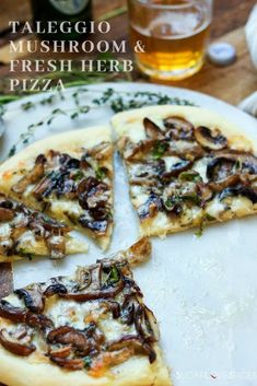 a white plate topped with slices of mushroom and fresh herb pizza next to a glass of beer