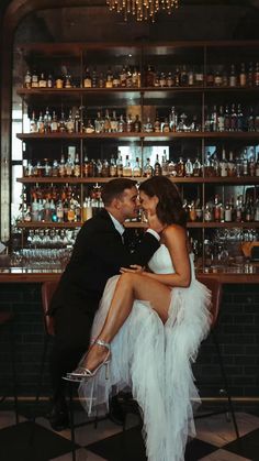 a bride and groom kissing in front of a bar with liquor bottles on the shelves