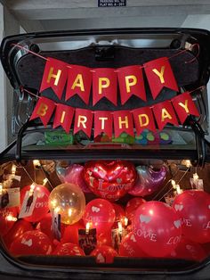 a trunk filled with lots of red balloons and some happy birthday signs hanging from it's sides