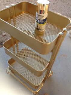 a gold metal cart with two shelves and a spray bottle on the bottom one shelf