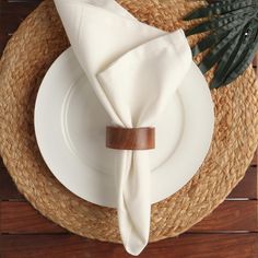 a place setting with white plates and napkins on a wooden tablecloth covered place mat