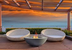 two white wicker chairs sitting on top of a wooden floor next to a fire pit