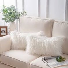 a white couch with two pillows on top of it next to a potted plant