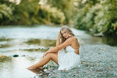 a beautiful woman sitting on top of a river bank