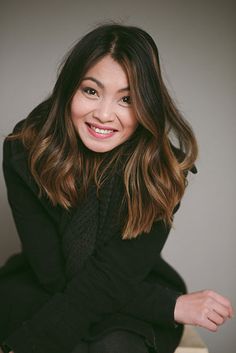 a smiling woman sitting on top of a wooden bench with her legs crossed and wearing black