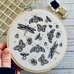 a person holding up a embroidery project with black and white butterflies on it's hoop