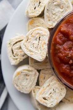 a white plate topped with rolls covered in tomato sauce and dipping sauce next to it