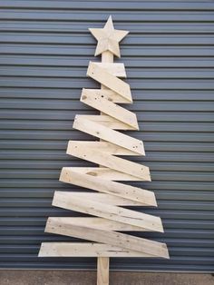 a wooden christmas tree made out of plywood planks on a metal wall in front of a garage door