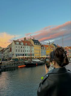 a woman taking a photo of some boats in the water and buildings on either side