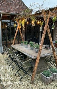 an outdoor dining area with potted plants on the table and lights hanging from the ceiling