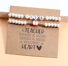 two white beaded bracelets with teacher's name and heart charms on them