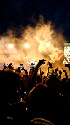 a crowd of people at a concert with their hands in the air and lights on