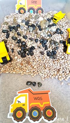 there are construction vehicles and rocks in the sand on this table with some sort of stickers