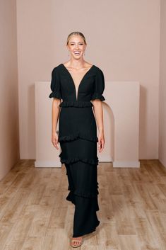 a woman in a green dress standing on a wooden floor with her hands behind her back