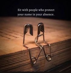 two pairs of metal scissors sitting on top of a wooden table next to a quote that reads sit with people who protect your name in your absentce