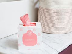 a pink tissue box sitting on top of a counter next to a white basket and some other items