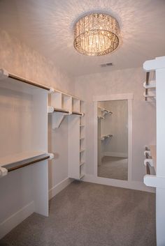 an empty walk - in closet with white walls and shelving unit, chandelier hanging from the ceiling