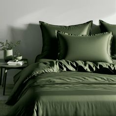 a bed with green sheets and pillows on top of it next to a night stand