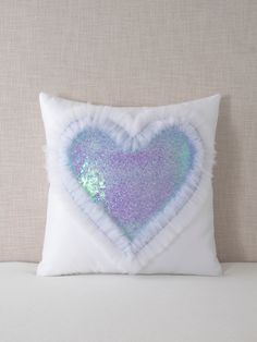 a white pillow with a blue and purple heart on the front, sitting on a bed