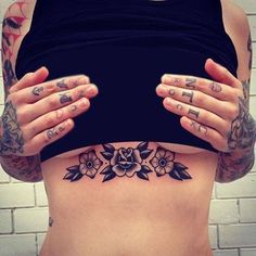 a woman with tattoos on her stomach holding her hands up to her chest and looking at the camera