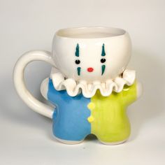 two ceramic mugs with faces on them sitting side by side, one is green and the other is blue