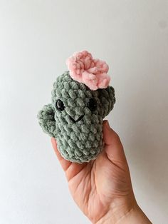 a hand holding a small green crocheted frog with a pink flower on its head