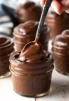 someone is spreading chocolate on top of some desserts in small glass jars with a spoon