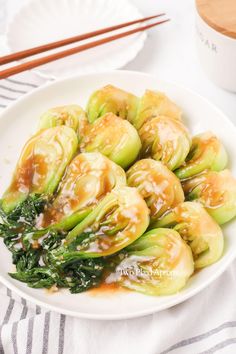 a white plate topped with brussel sprouts covered in sauce next to chopsticks