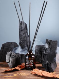 a bottle filled with reeds sitting on top of a wooden table next to rocks