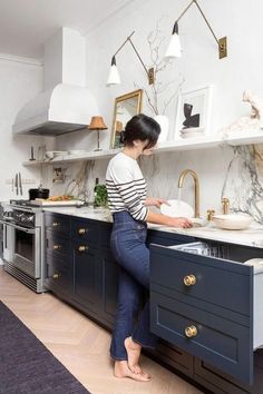 a woman standing in front of a kitchen sink with an open drawer on the counter