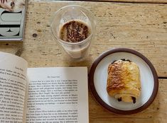 an open book sitting on top of a wooden table next to a plate with food