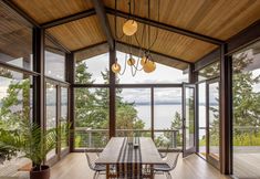 a dining room with large windows overlooking the water and trees in the distance is shown