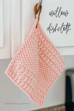 a pink crocheted dish cloth hanging from a hook on a kitchen cabinet door