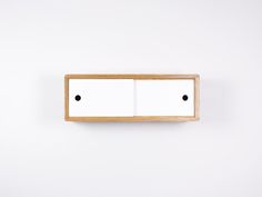 a white cabinet with two black dots on the front and one is open, against a white wall