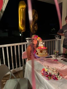 a woman sitting at a table with a cake on it and balloons in the air