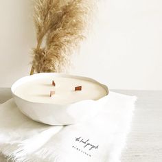 a white bowl sitting on top of a table next to a dried plant