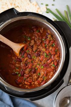 a wooden spoon in a pot full of chili and beans with tortilla chips on the side