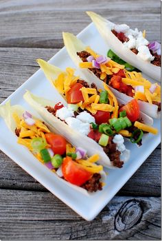 three tacos on a white plate topped with cheese, tomatoes and other toppings