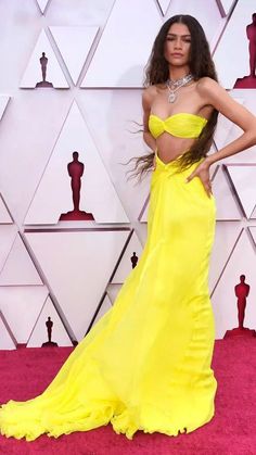 a woman in a yellow dress standing on a red carpet with her hands on her hips